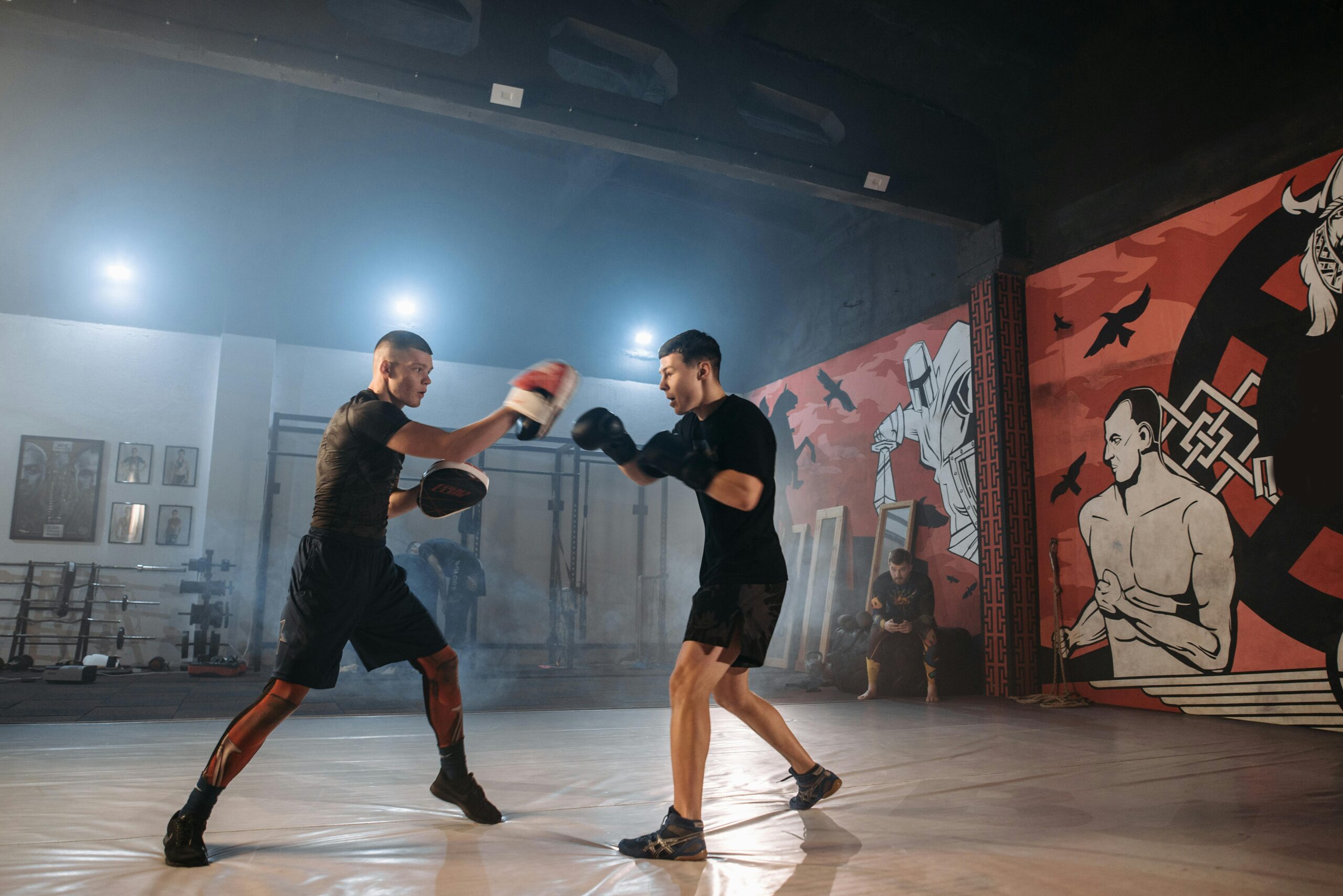 Two men practicing martial arts training in a stylish gym with vivid murals and equipment.